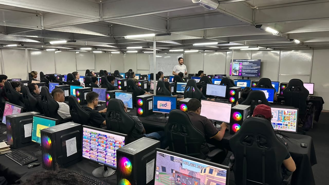 Instrutor diante de telão com o tema 'use plataformas e apps para encontrar trabalho' e alunos em computadores