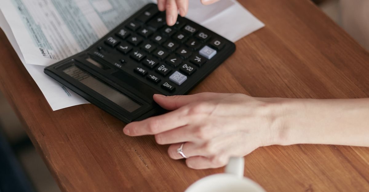 Mãos de uma pessoa sobre uma calculadora e papéis de contas em uma mesa de madeira