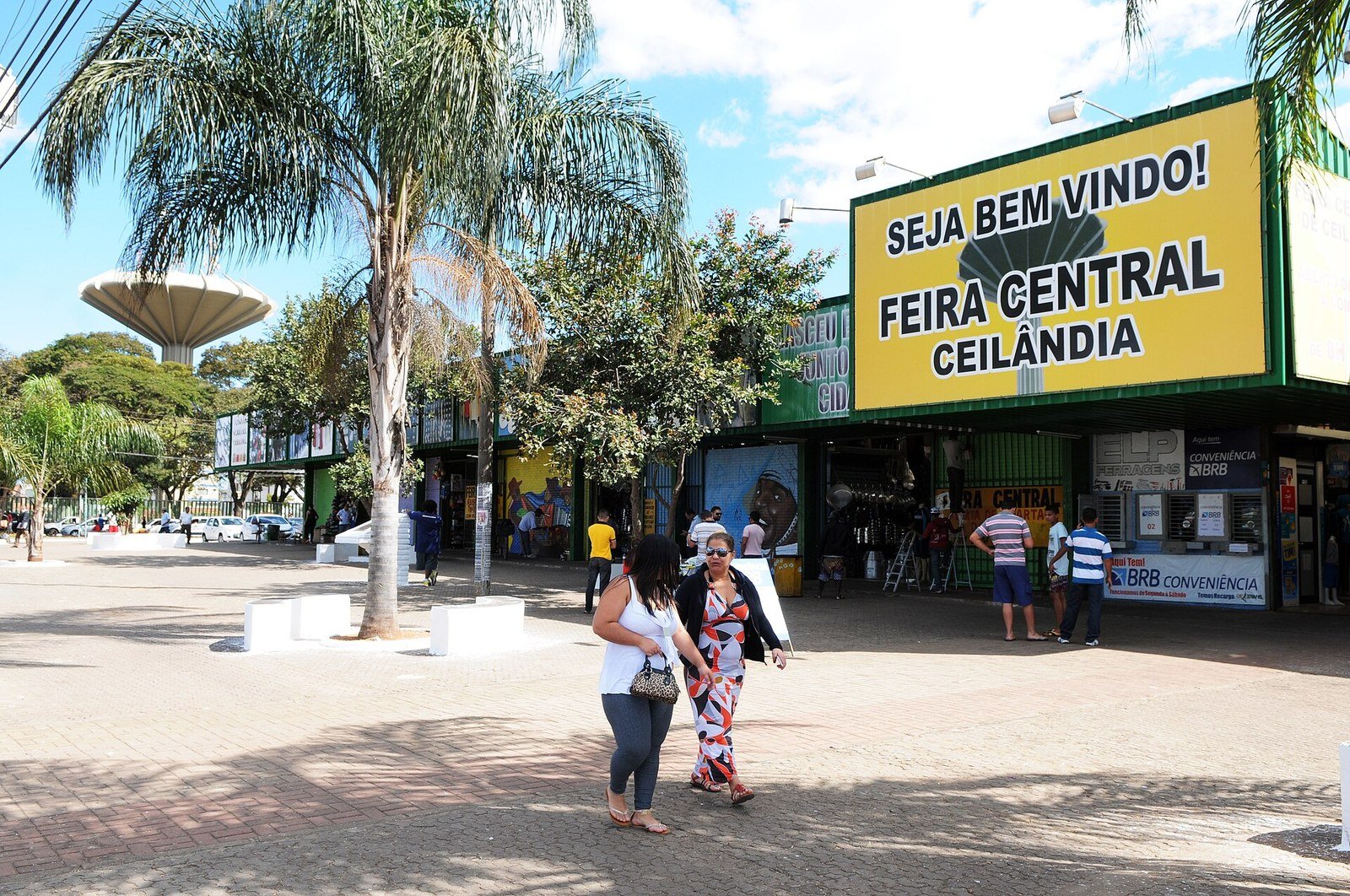 Fachada da Feira Central de Ceilândia, com lojas abertas e pedestres circulando, no Distrito Federal