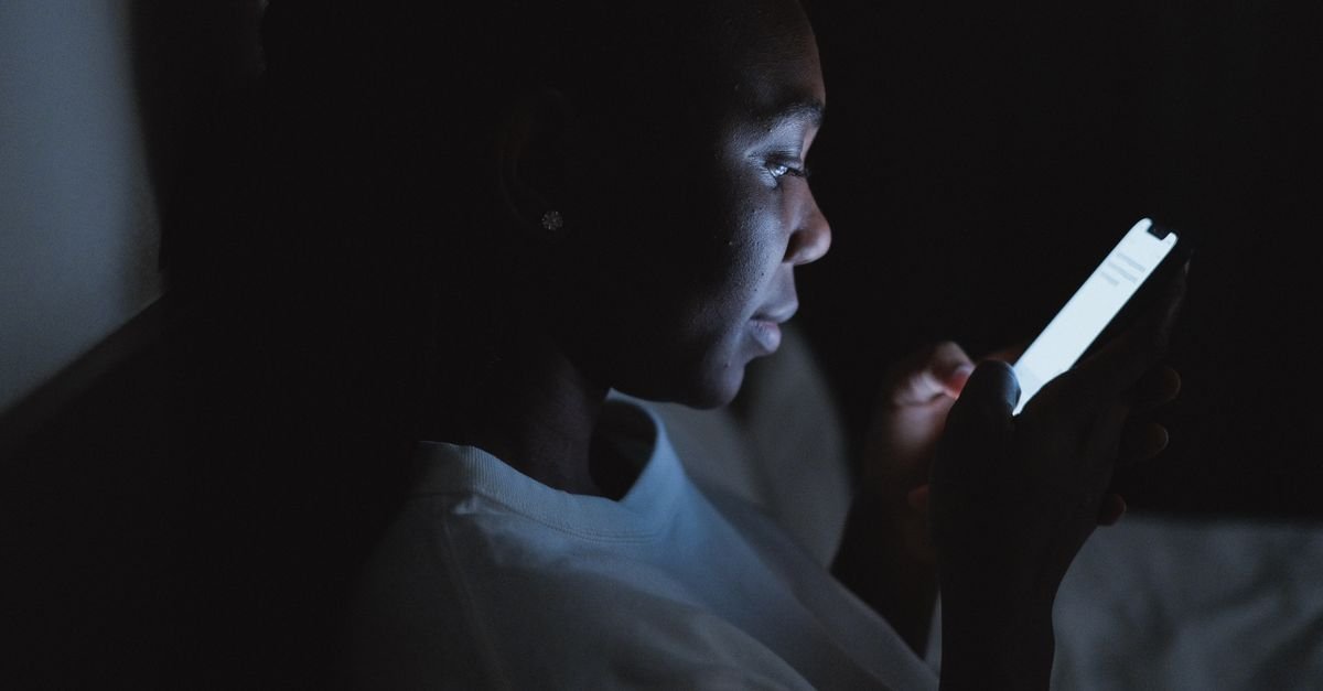 Mulher usa celular no escuro, iluminada apenas pela tela do aparelho