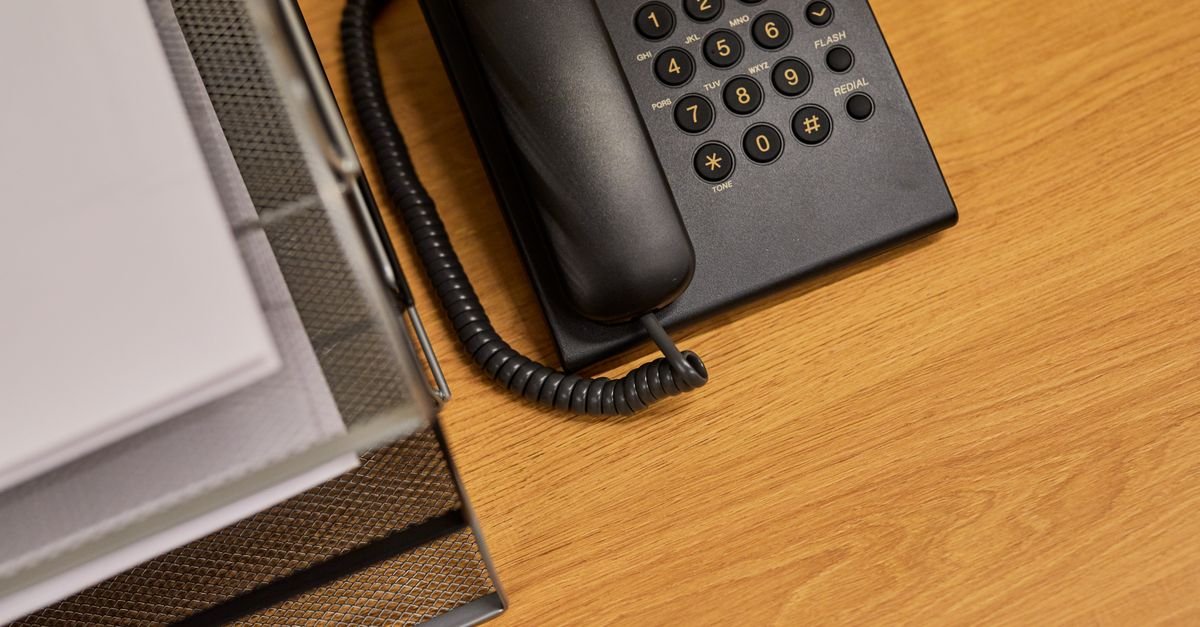 Telefone fixo preto sobre mesa de escritório ao lado de bandeja com documentos