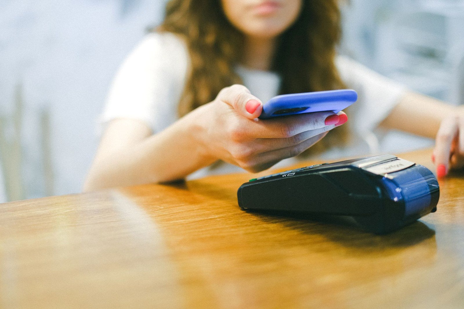 Mulher aproxima o celular de uma maquininha de pagamento sobre uma mesa de madeira