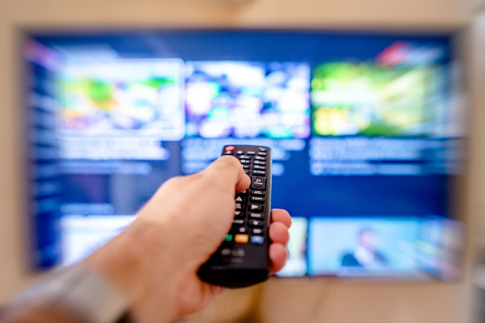 Mão segurando controle remoto diante de televisão com catálogo de streaming desfocado