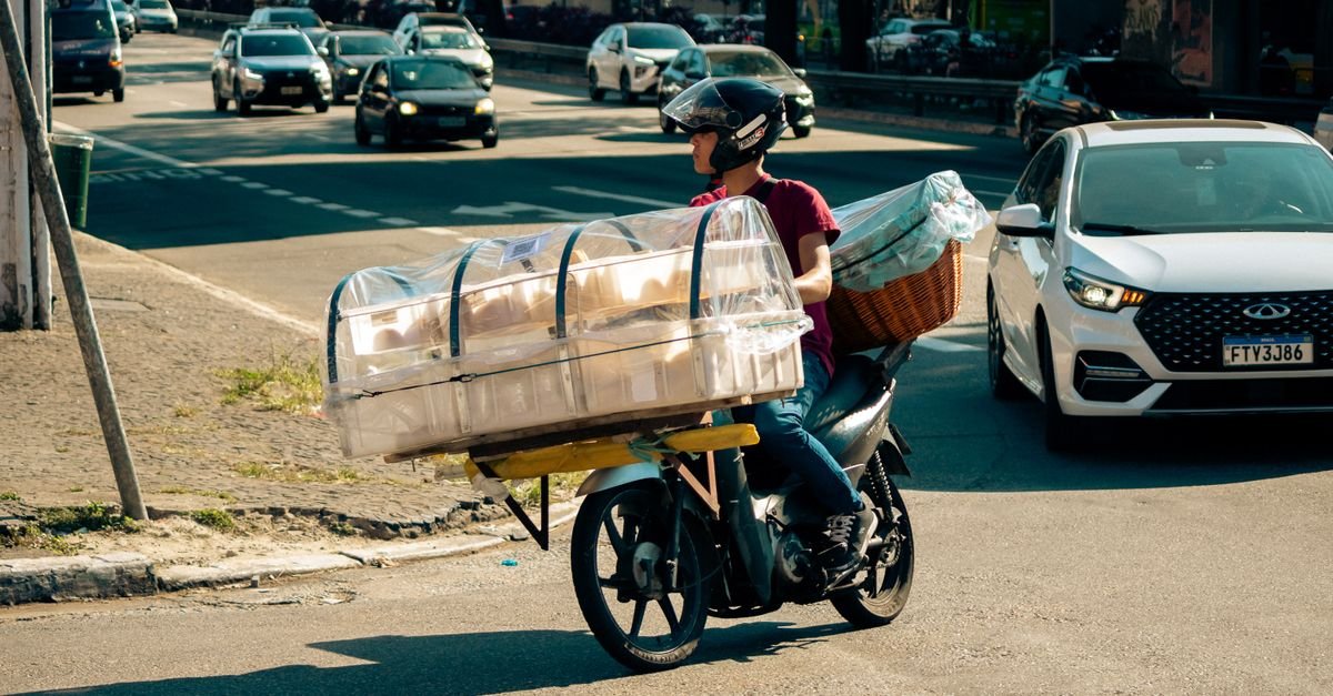 Motociclista transporta carga em avenida movimentada durante o dia