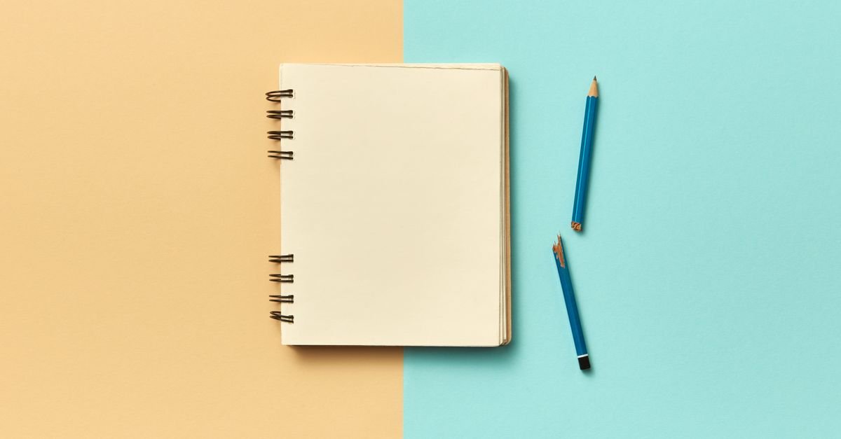 Caderno de capa branca fechado sobre fundo bege e azul, ao lado de um lápis azul partido ao meio