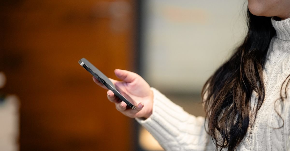 Mao de uma mulher segurando um telefone celular em ambiente interno