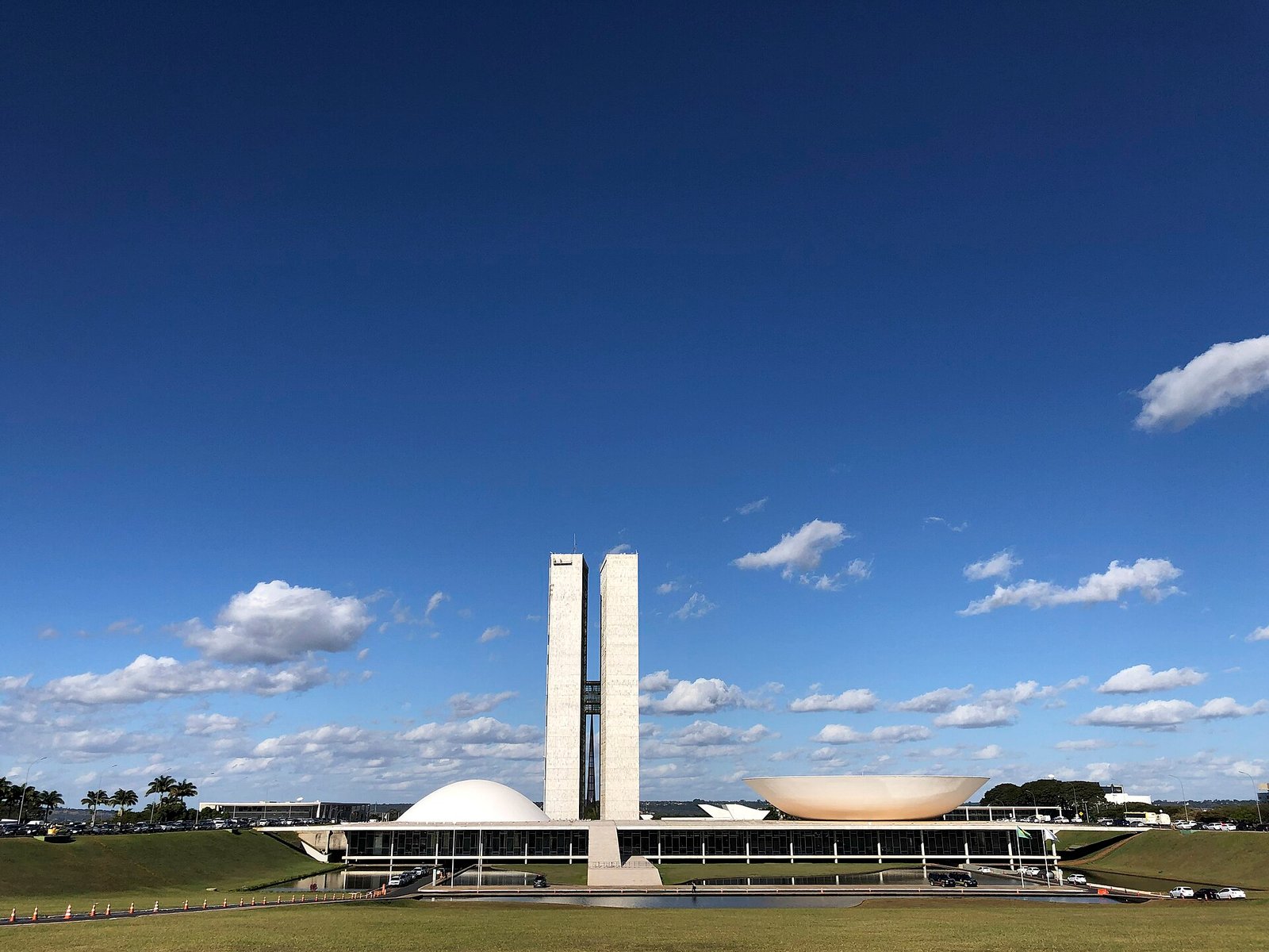 Fachada do Congresso Nacional em Brasília, com as duas torres, a cúpula e o espelho d'água, em dia de céu azul