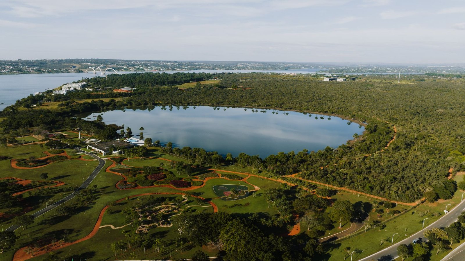Vista aérea do Lago Paranoá e de áreas verdes de Brasília, com a Ponte JK ao fundo