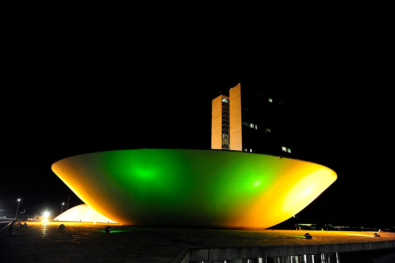 Congresso Nacional iluminado em verde e amarelo à noite, com a cúpula do Senado em primeiro plano