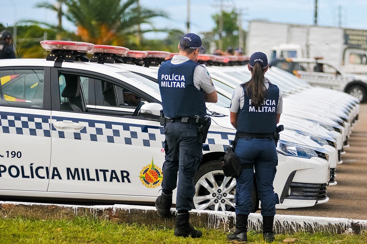 Policiais militares do Distrito Federal ao lado de fileira de viaturas brancas com a inscrição Polícia Militar