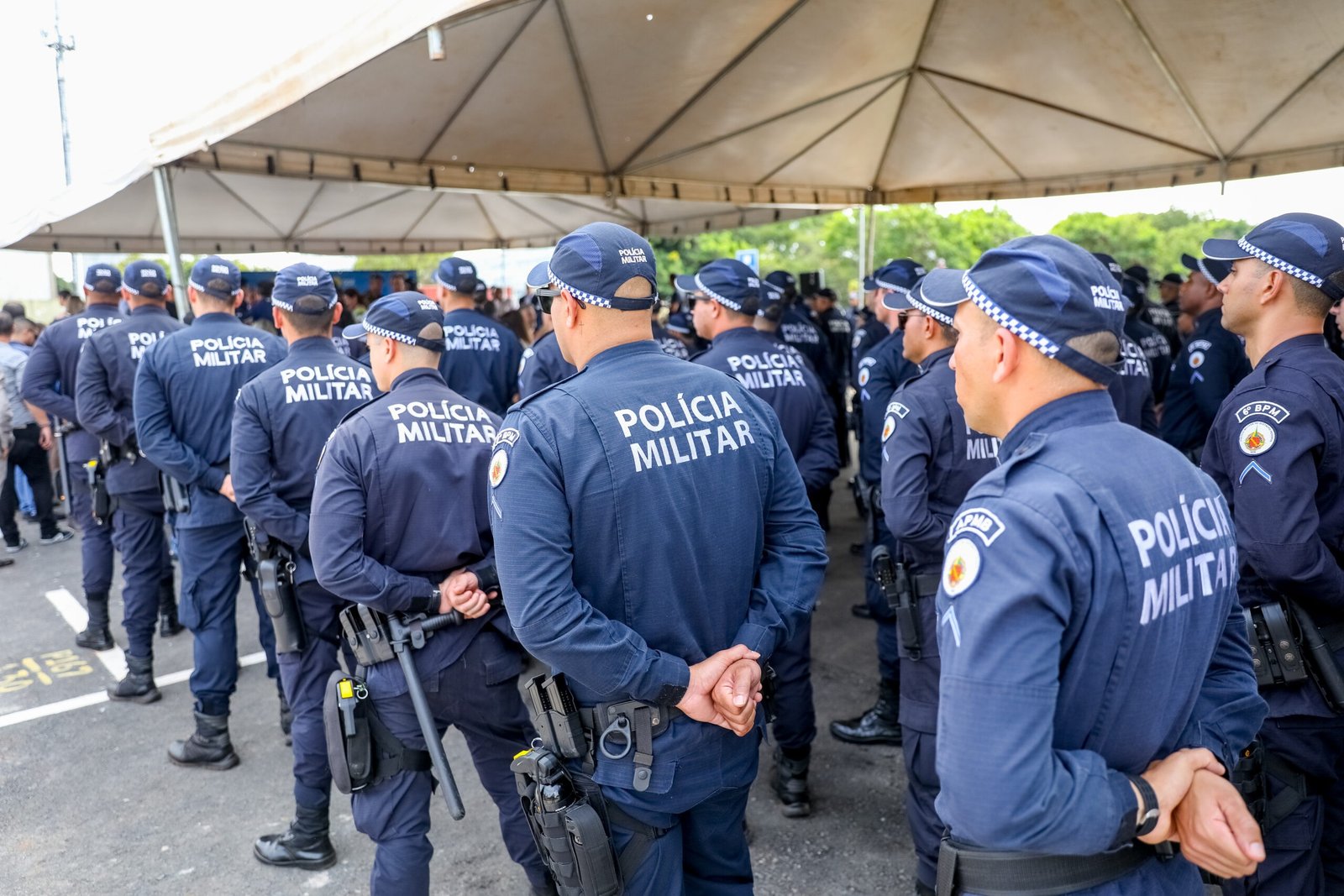Policiais militares do DF em formatura sob tenda, de costas, com cassetete e equipamentos na cintura; foto de arquivo
