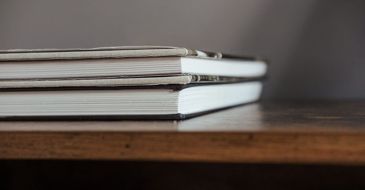 Dois livros de capa dura empilhados sobre uma prateleira de madeira