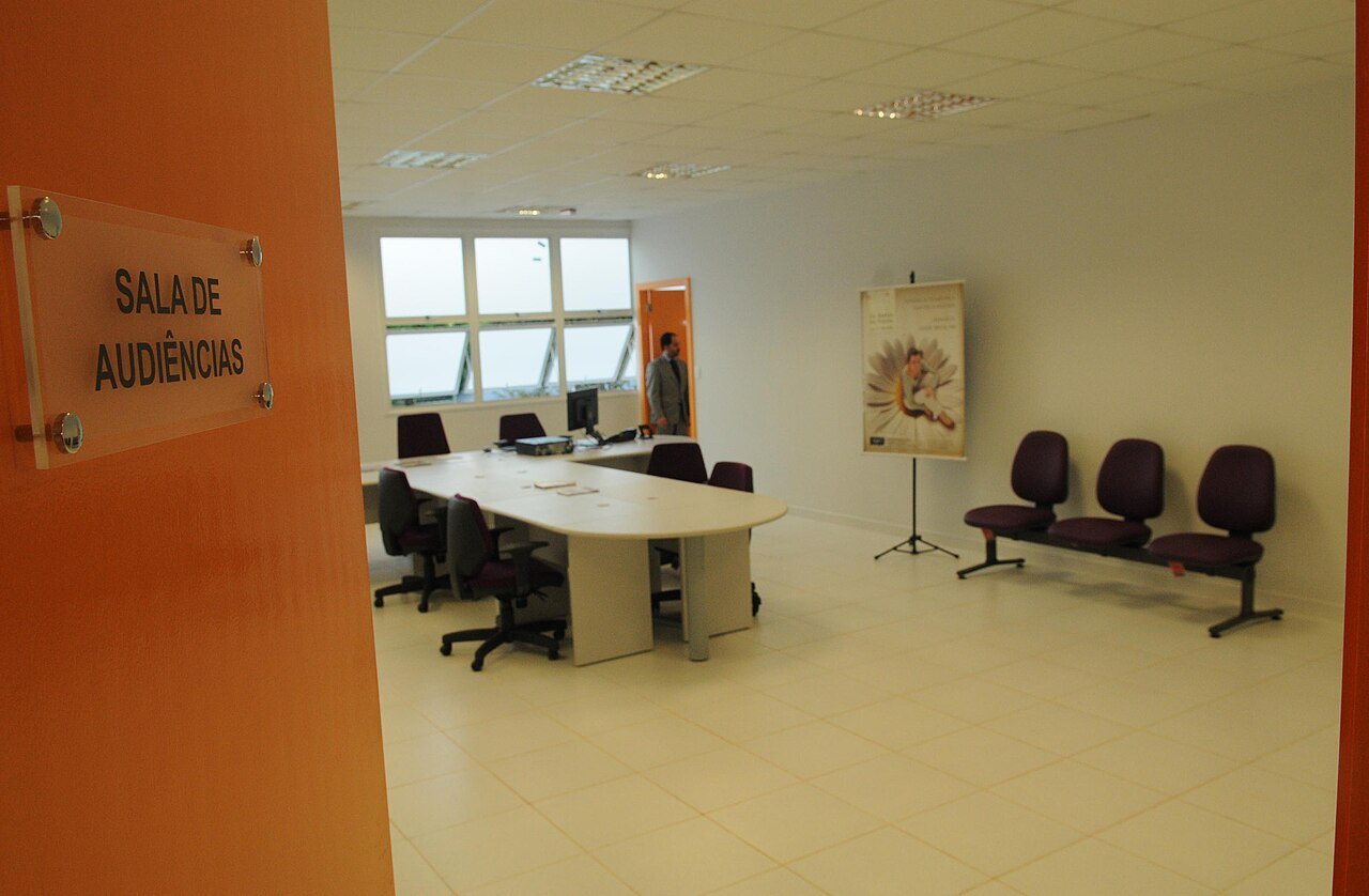 Sala de audiências da Casa da Mulher Brasileira, em Brasília, com mesa, cadeiras e placa na porta