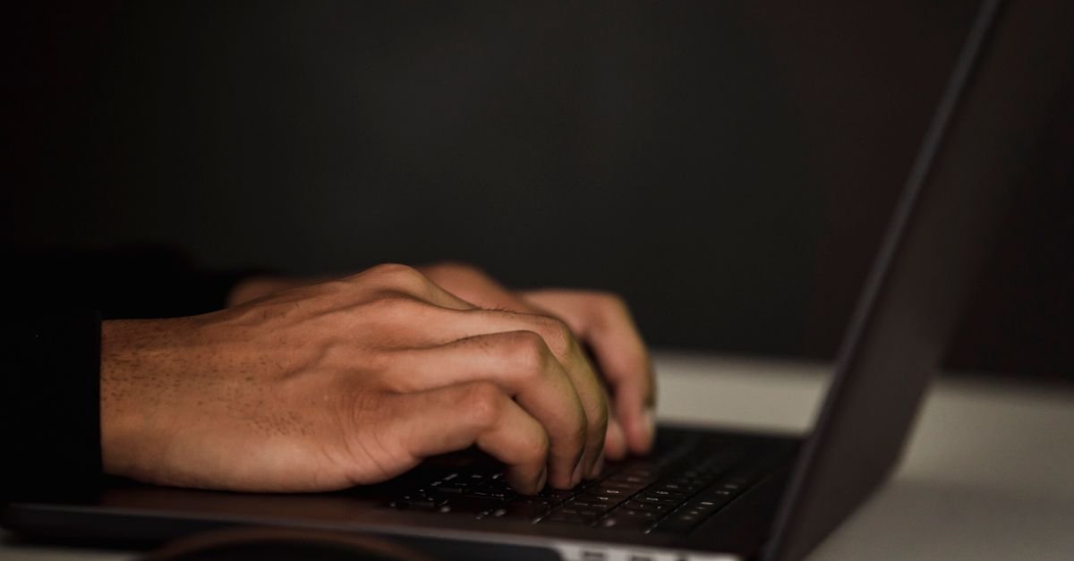 Maos de uma pessoa digitando no teclado de um notebook em ambiente escuro