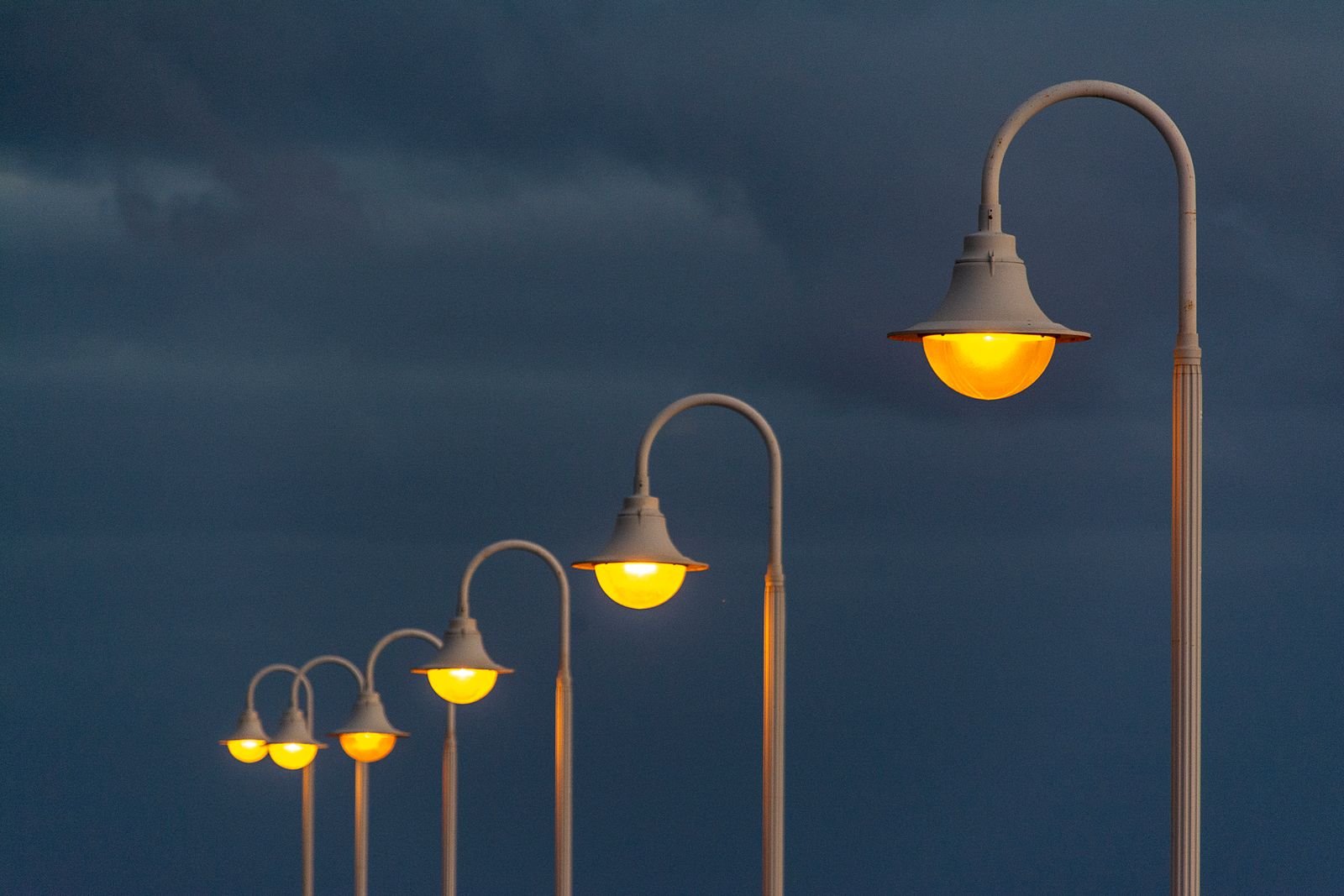 Fileira de postes de iluminação pública com lâmpadas acesas ao entardecer, foto ilustrativa de arquivo