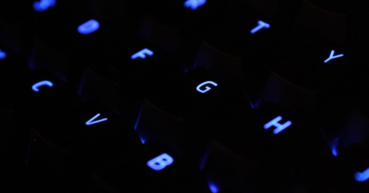 Teclado de computador com teclas iluminadas em azul no escuro