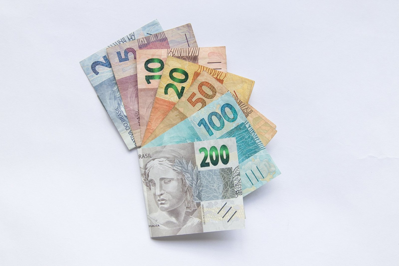 Cédulas de Real de R$ 2 a R$ 200 dispostas em leque sobre fundo branco; foto ilustrativa