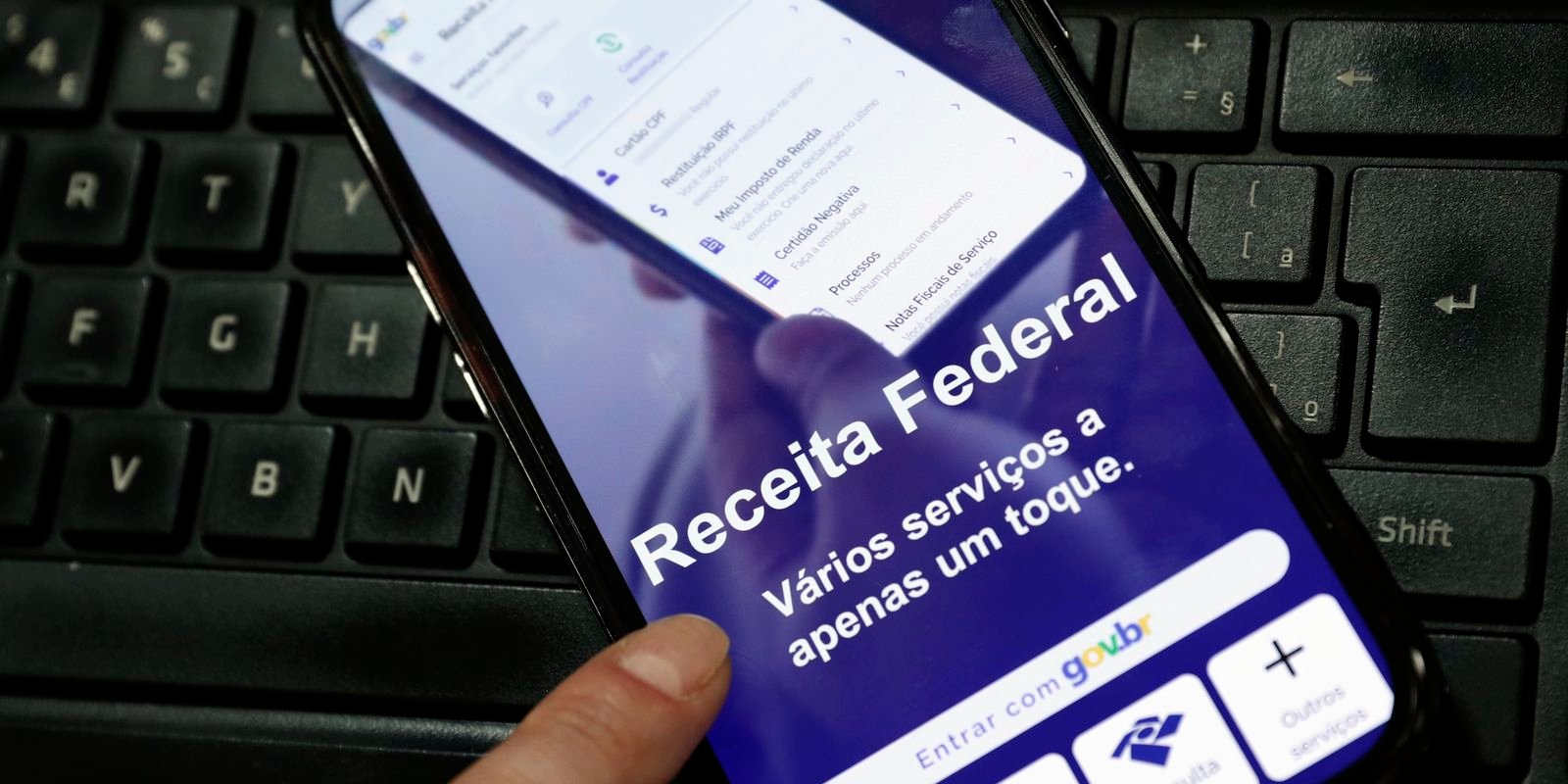 Celular com o aplicativo da Receita Federal aberto, apoiado sobre um teclado, em foto de arquivo