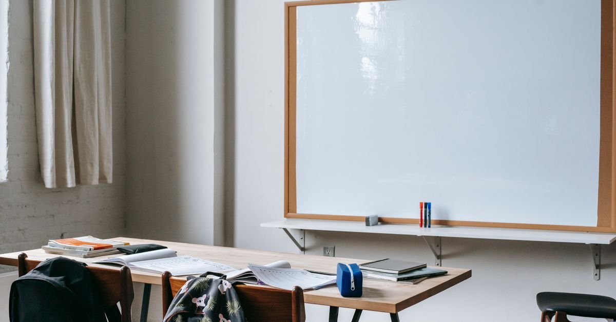 Sala de aula vazia com carteira, cadernos e material escolar sobre a mesa