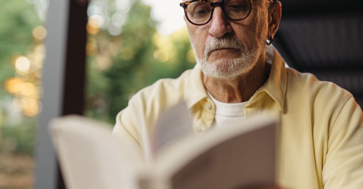 Homem idoso de óculos lendo um livro aberto ao ar livre