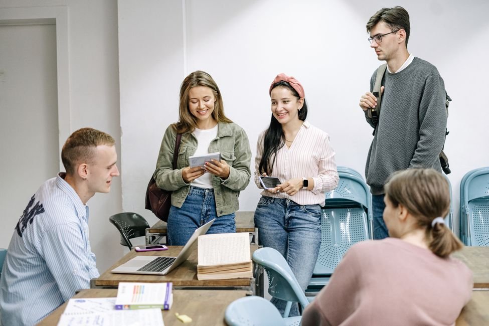 Grupo de estudantes universitarios reunidos em torno de uma mesa com laptop e livros em sala de aula