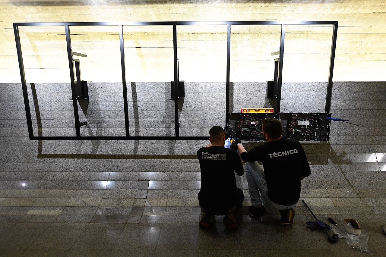 Dois tecnicos agachados instalam painel eletronico em parede de granito no interior do Senado Federal