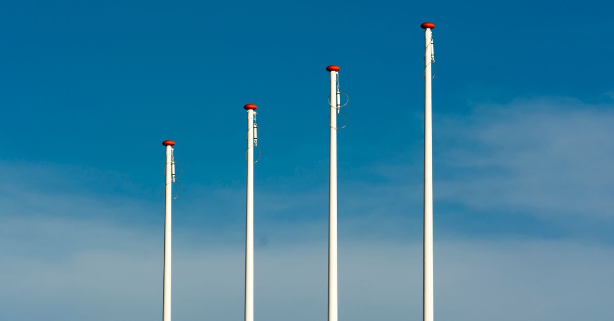 Quatro mastros de bandeira sem bandeiras sob céu azul