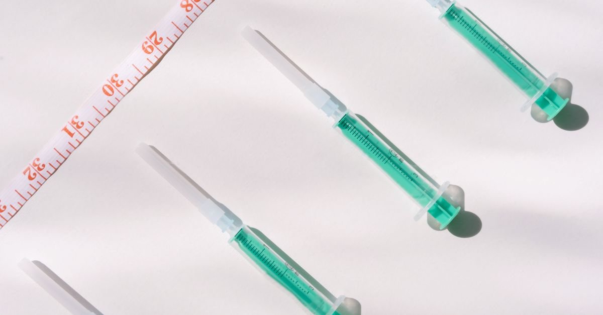 Seringas com líquido verde ao lado de fita métrica sobre fundo branco