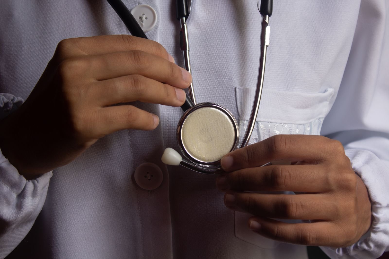 Médico segurando o estetoscópio em close, com jaleco branco