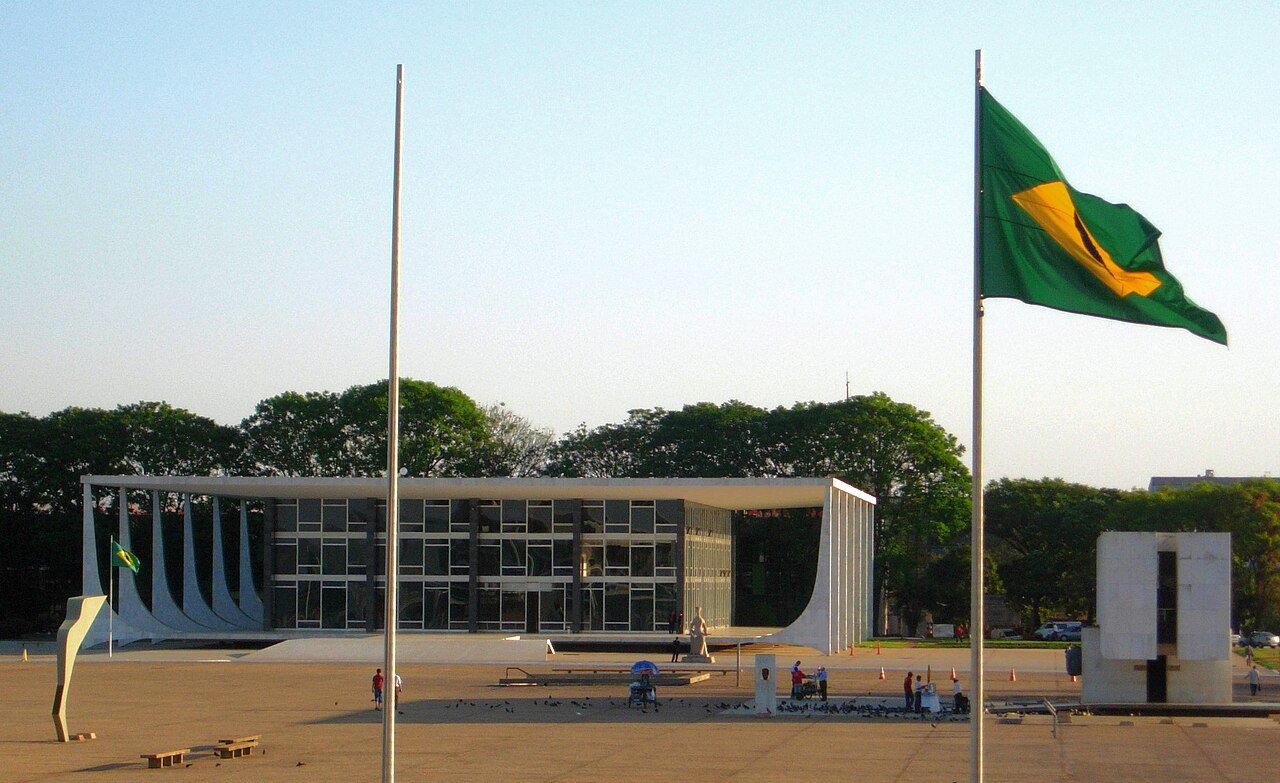 Fachada do edifício do Supremo Tribunal Federal vista da Praça dos Três Poderes, em Brasília, com a bandeira do Brasil hasteada em primeiro plano
