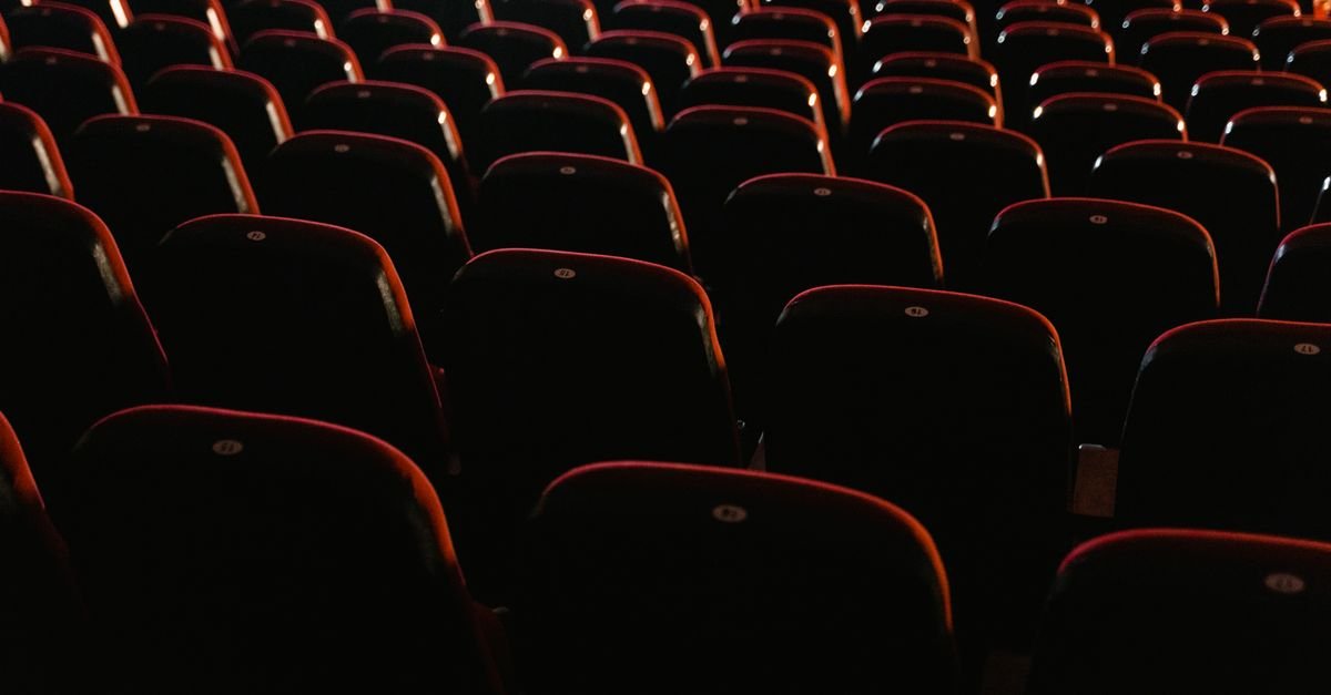 Fileiras de poltronas vermelhas vazias em uma sala de cinema com iluminação baixa