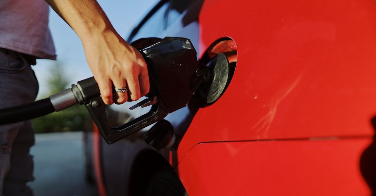 Mão segura o bico de combustível durante abastecimento de um carro vermelho em um posto