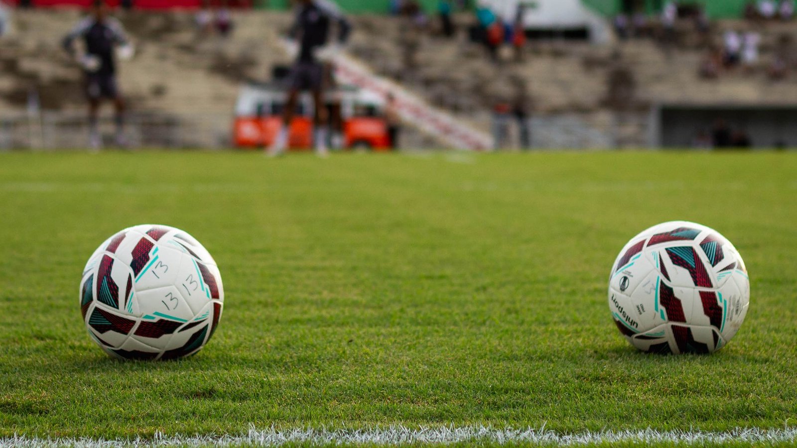 Duas bolas de futebol sobre o gramado de um estádio, com a linha lateral em primeiro plano