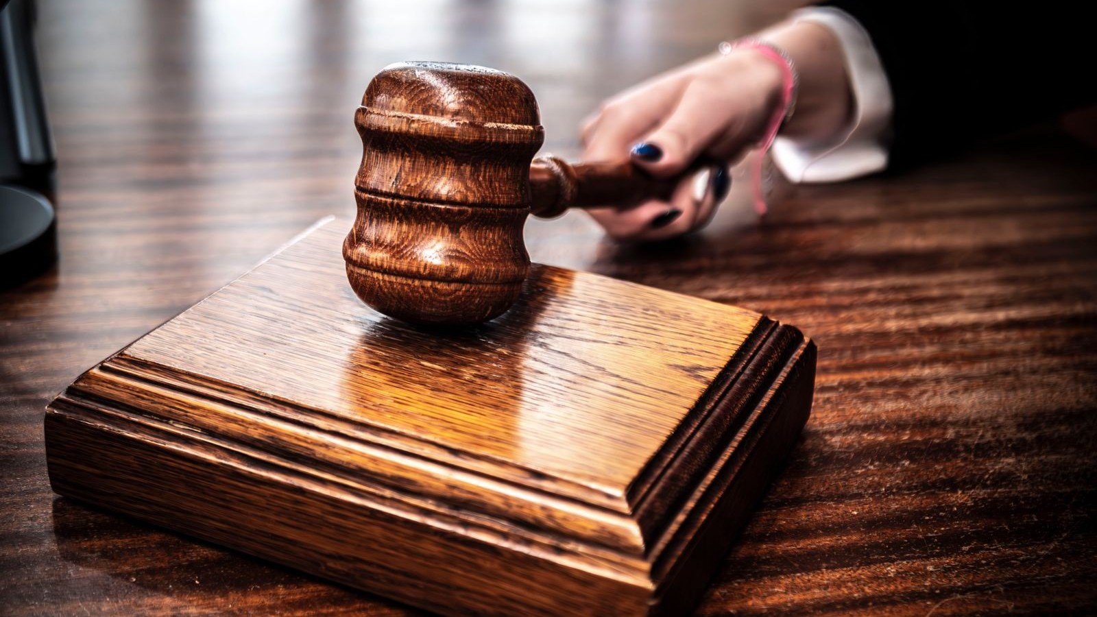 Martelo de madeira de juiz apoiado sobre base, em mesa de tribunal, foto ilustrativa