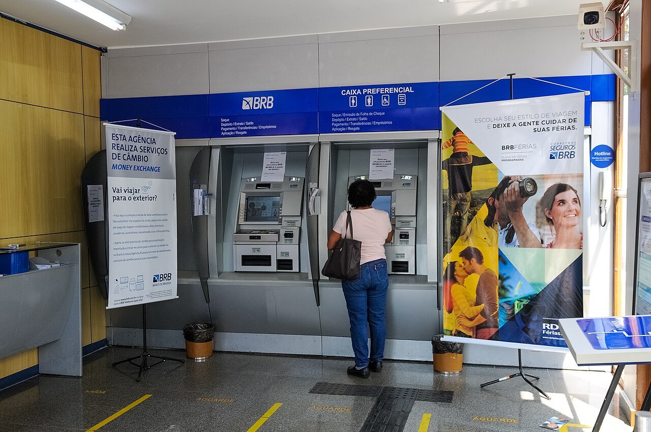 Interior de agência do BRB com caixas eletrônicos e uma cliente de costas