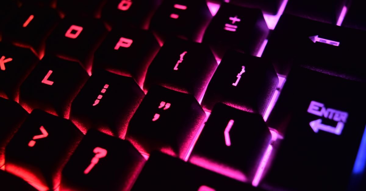 Close-up de teclado mecânico com iluminação vermelha e rosa em ambiente escuro