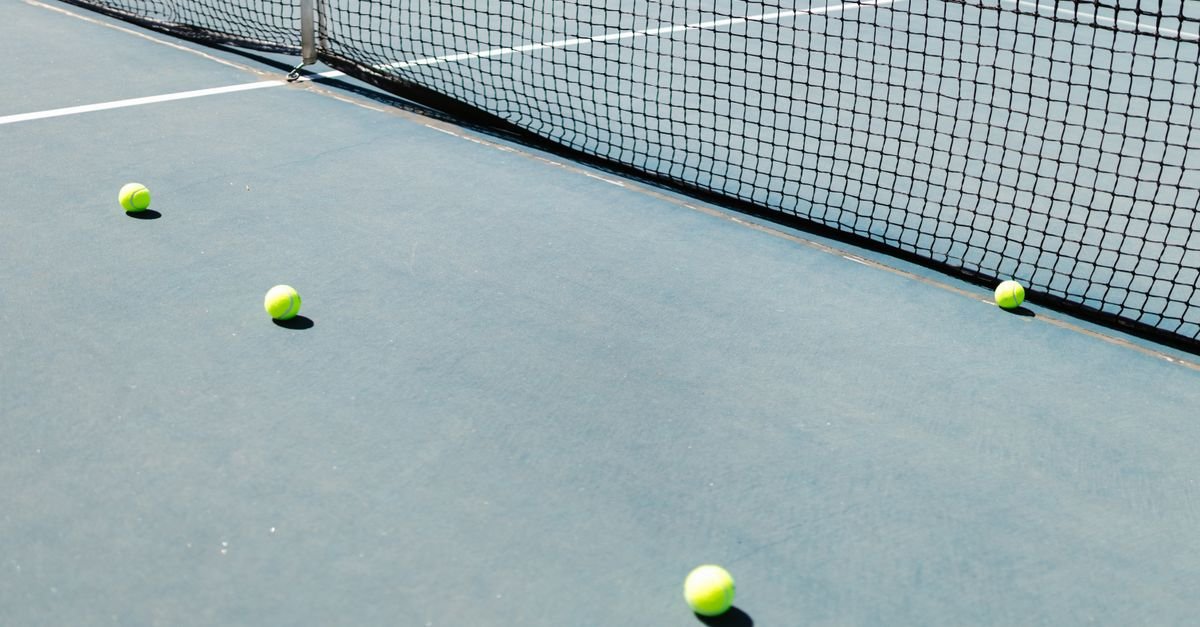 Quadra de tenis com rede e bolas espalhadas no piso