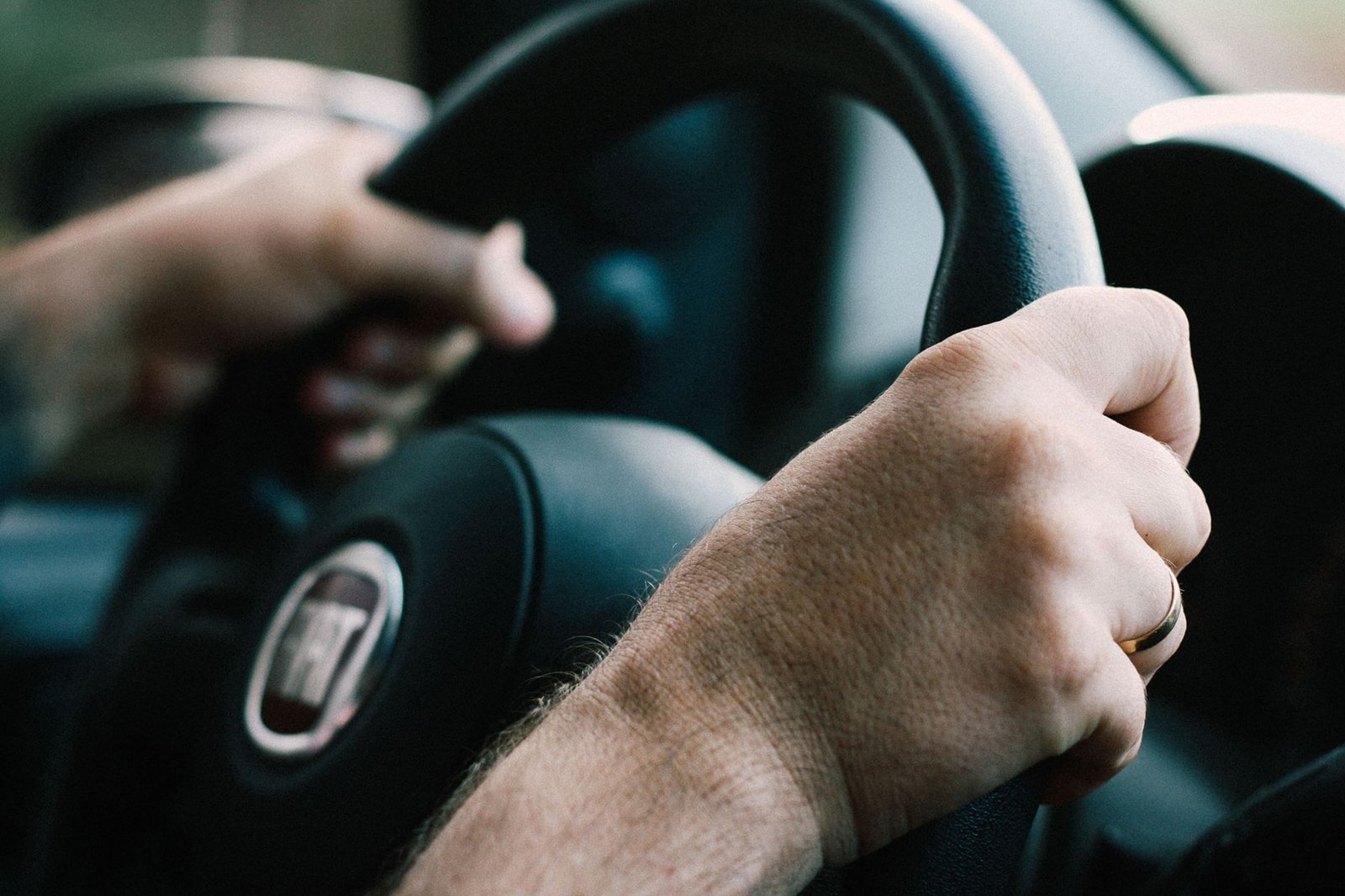 Duas mãos seguram o volante de um carro durante a condução, em primeiro plano