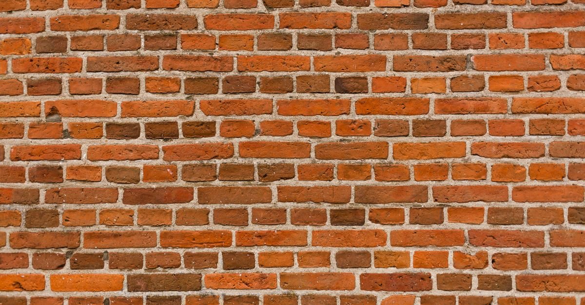 Muro de tijolos vermelhos aparentes visto de frente, com juntas de argamassa cinza