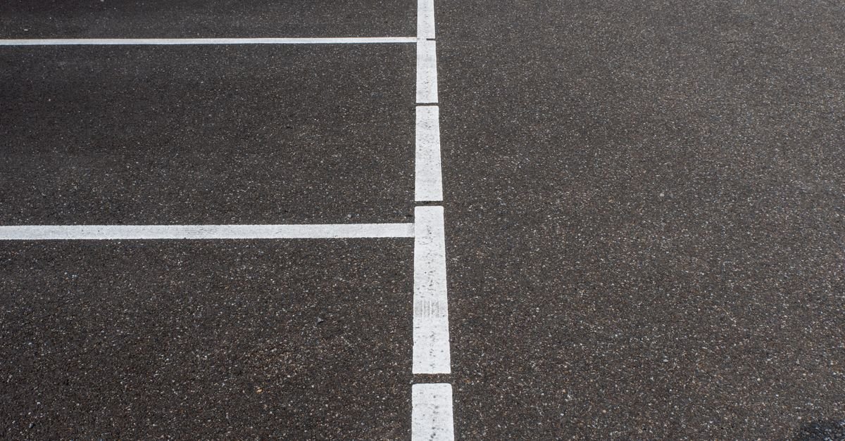 Vaga de estacionamento vazia demarcada com faixas brancas sobre asfalto