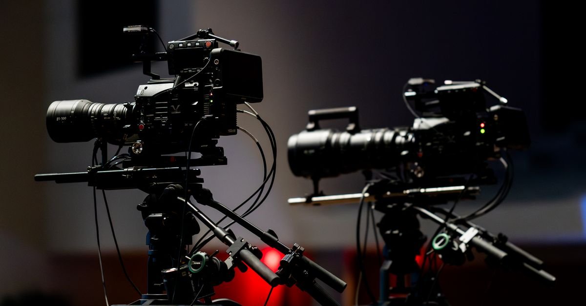 Duas câmeras de televisão profissionais montadas em tripés dentro de um estúdio