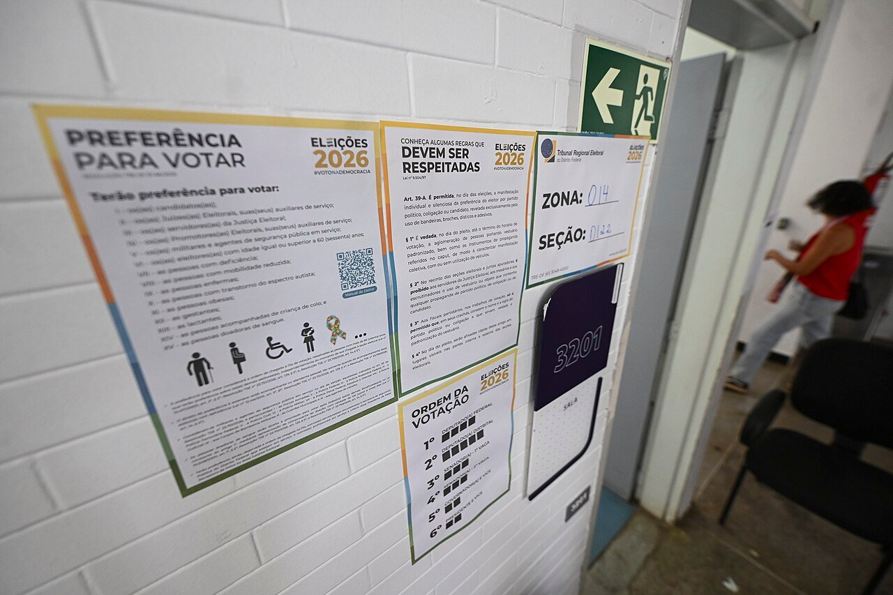 Cartazes do TRE-DF com zona e seção na porta de uma sala de votação em Brasília, no primeiro turno de 2026