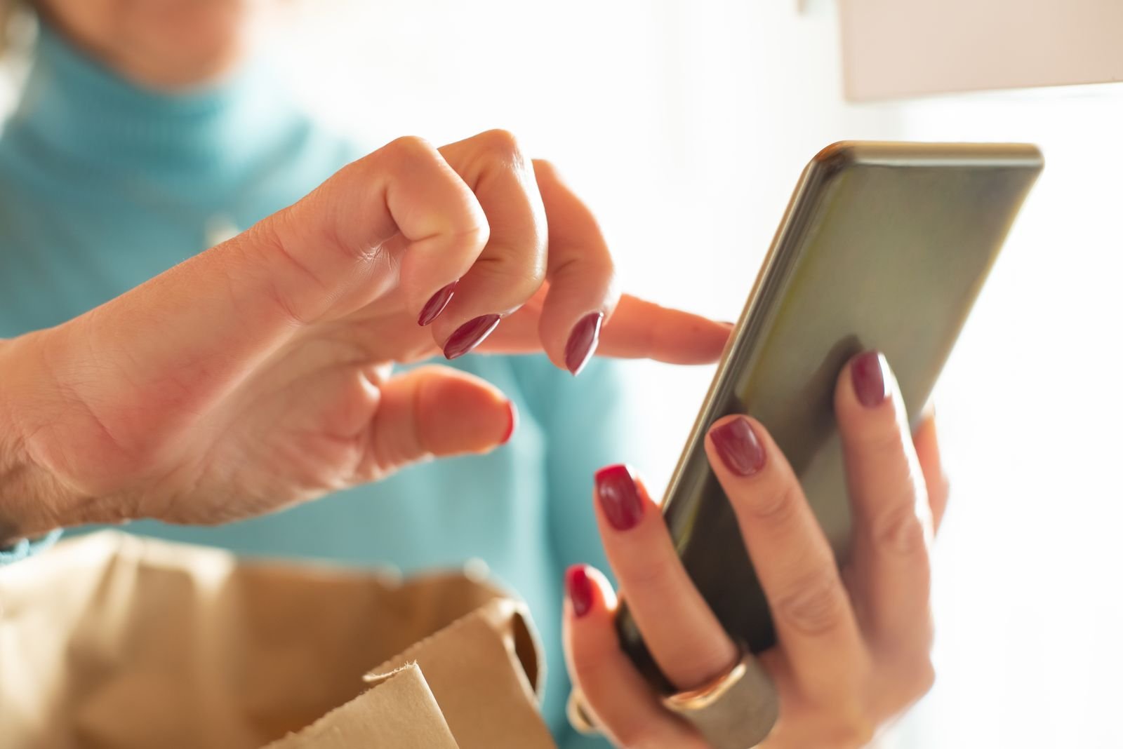 Mãos de uma mulher usam um smartphone, com sacola de papel em primeiro plano