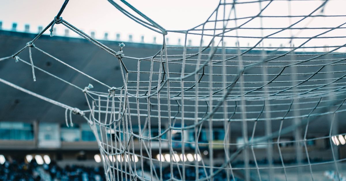 Rede de gol de futebol em primeiro plano com arquibancada de estadio ao fundo