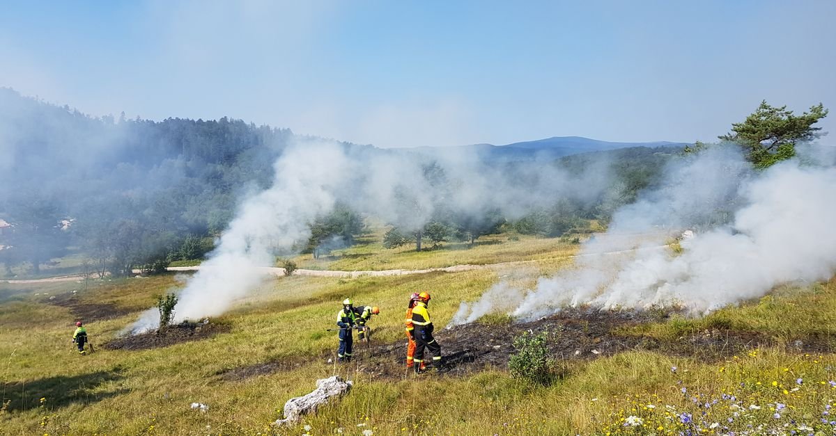 Bombeiros combatem fogo em vegetação rasteira com fumaça densa cobrindo a encosta