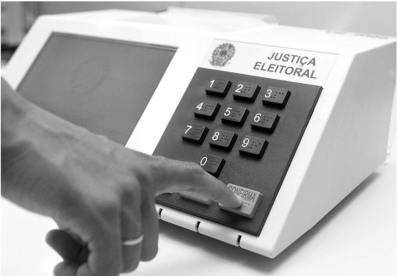 Dedo pressiona a tecla confirma de uma urna eletrônica da Justiça Eleitoral