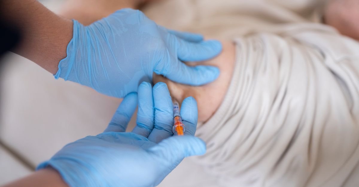 Profissional de saúde com luvas azuis aplica injeção no braço de um paciente