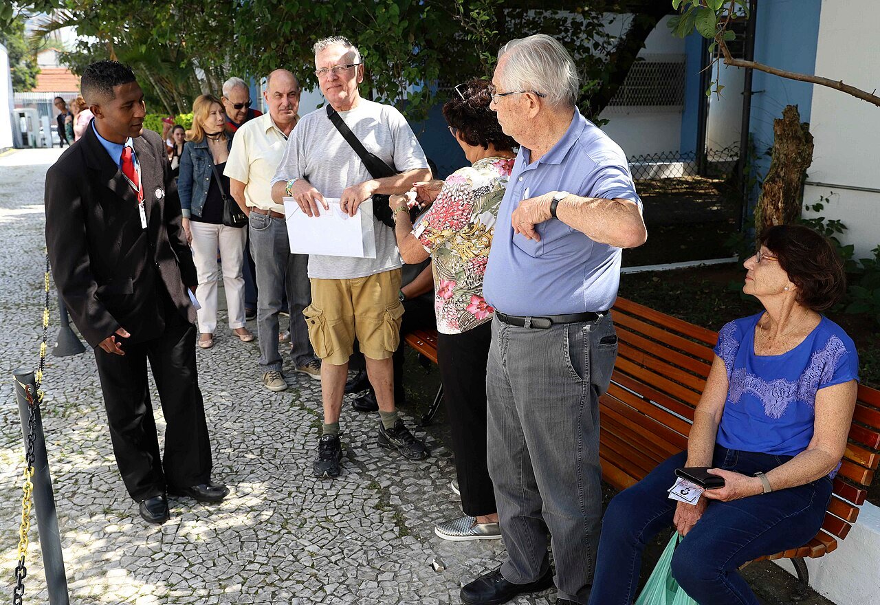 Pessoas aguardam em fila do lado de fora de uma unidade de saúde durante campanha de vacinação, com agente de saúde orientando o público